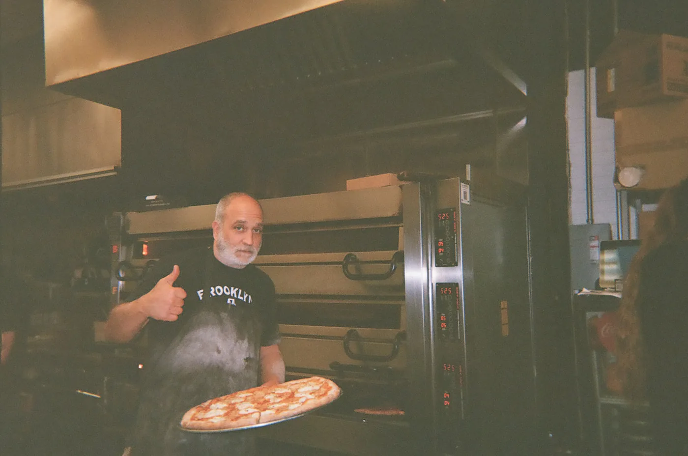 Brooklyn City pizzaiolo holding a fresh pie